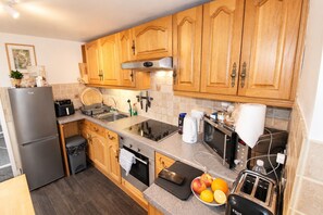 A compact kitchen with wooden cabinets, a built-in oven, a microwave, and a toaster. - Carlton Cottage Keswick -  a cottage that sleeps 2 guests  in 1 bedroom (Keswick)