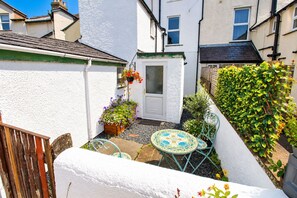 A small courtyard with a white door, a wooden fence, a table with chairs, and potted plants.