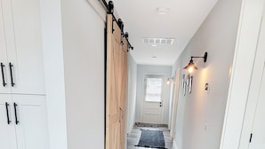 Un couloir aux murs blancs, doté d’un plancher en bois et d’une porte coulissante de style rustique.