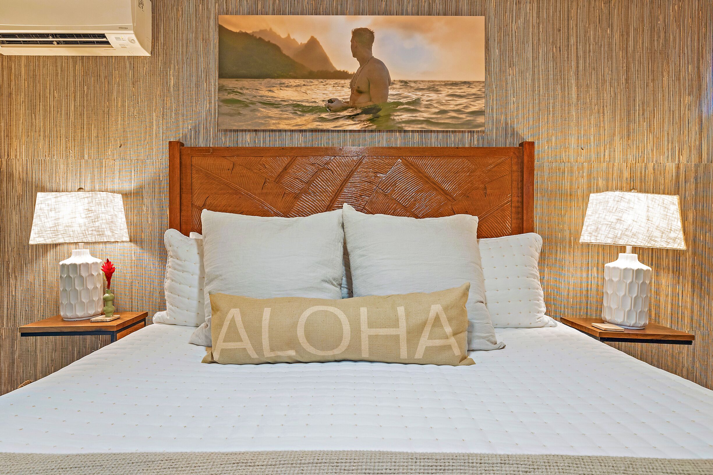 Een hotelkamer met een groot bed, een houten hoofdbord, twee nachtkastjes met lampen en een schilderij van een persoon in het water.