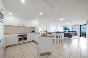 A modern kitchen with white cabinetry, a built-in oven, and a dining area with a table and chairs. - Airlie Horizon (Airlie Beach)