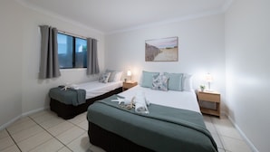 Una camera d'albergo con due letti, una finestra con tende, un quadro appeso al muro e un comodino con una lampada.
