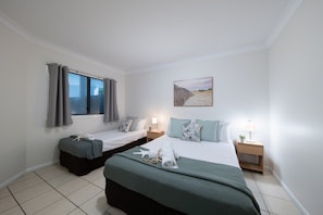 A hotel room with two beds, a window with curtains, a painting on the wall, and a bedside table with a lamp. - Airlie Horizon (Airlie Beach)