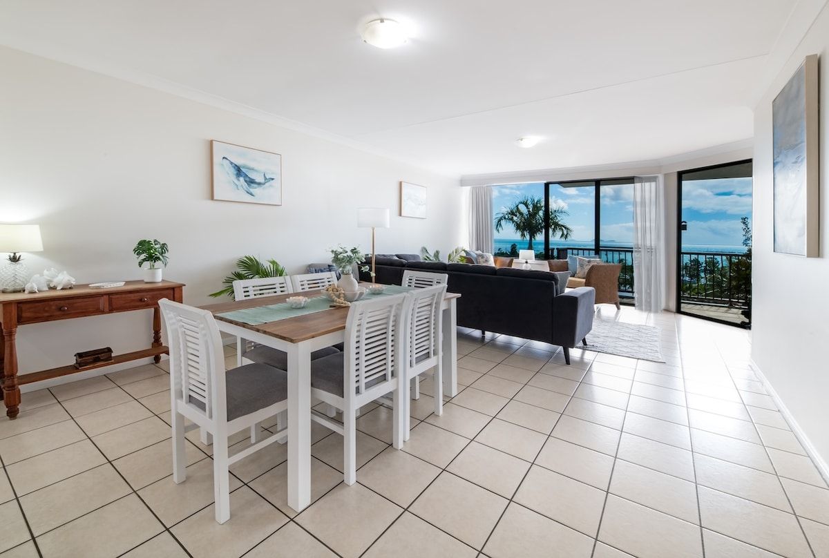 A modern living room with a dining area, large windows, and a balcony with a view.