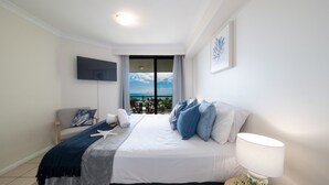 Una camera d'albergo con un letto, una TV a parete, una finestra con vista e un comodino con lampada.