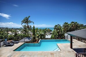 A swimming pool with a view of the ocean, surrounded by palm trees and a clear sky. - Airlie Horizon (Airlie Beach)