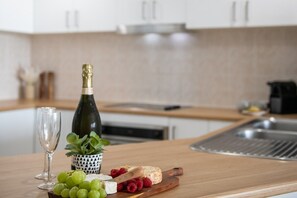A kitchen counter with a bottle of champagne, a glass, grapes, raspberries, and a cheese board. - Airlie Horizon (Airlie Beach)