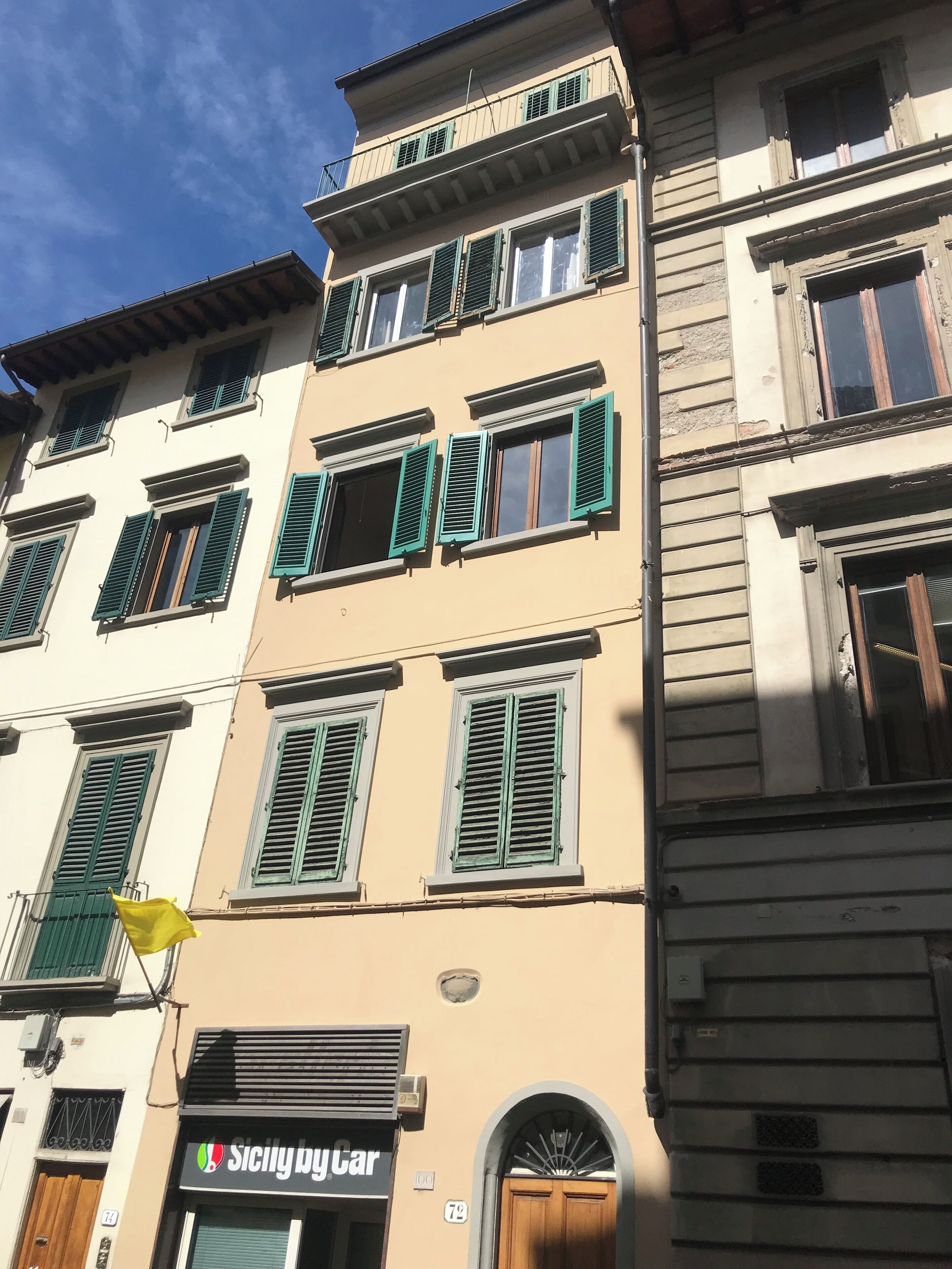 Un edificio a più piani con persiane verdi, un negozio con insegne ben visibili e un cielo sereno.