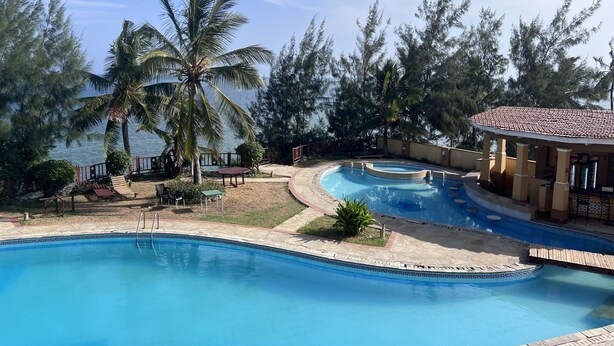 A pool area with a view of the sea, surrounded by palm trees and a covered seating area. - Magical Beachfront Apartments (Mombasa)