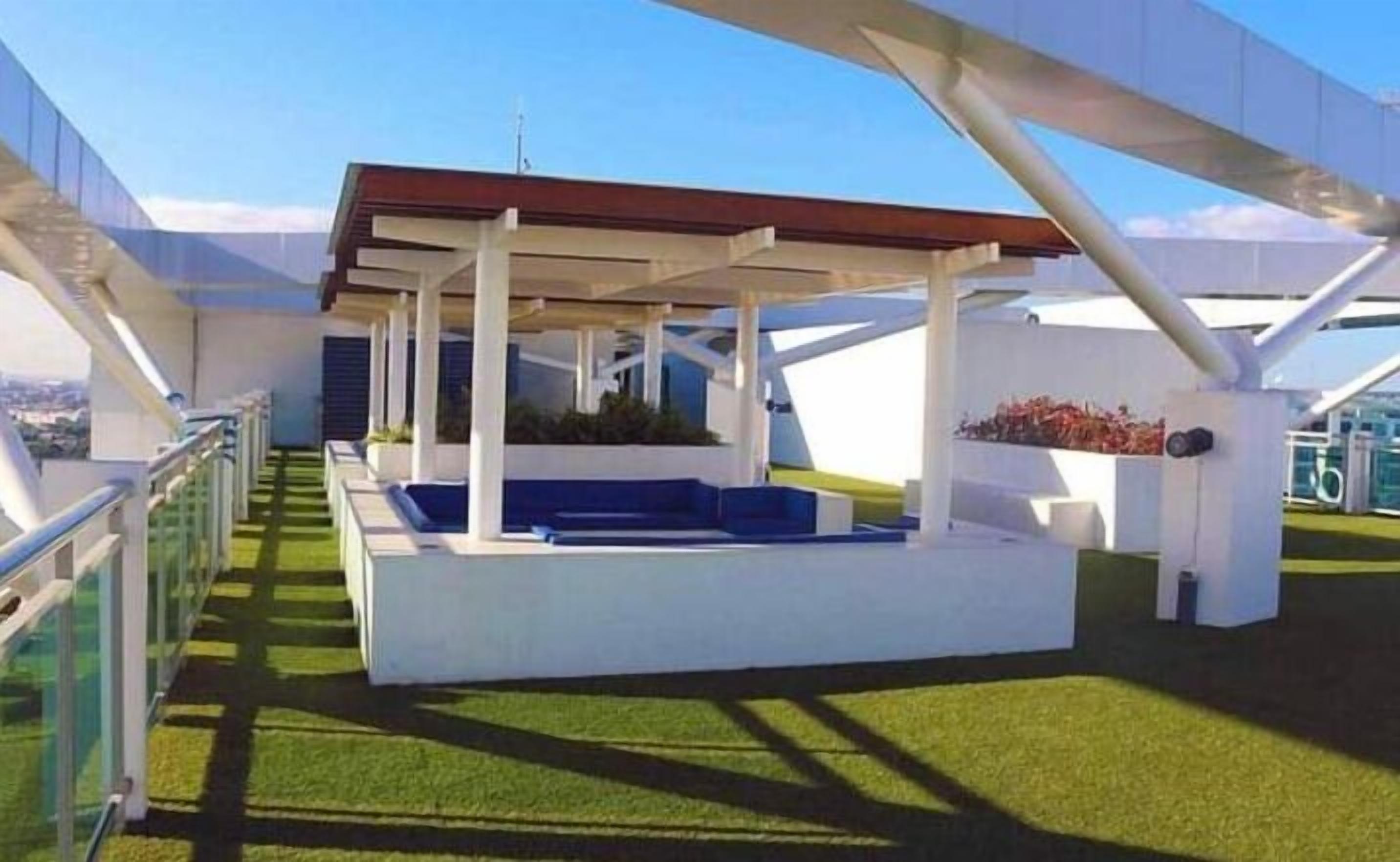 A modern outdoor seating area with a white structure, blue cushions, and a red roof.