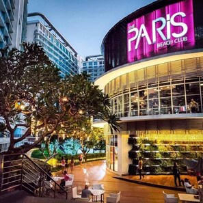 Il Paris Beach Club, con una moderna facciata in vetro, area salotto esterna e una piscina visibile.