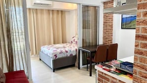 Una habitación moderna con cama, una mesa de comedor con sillas, un televisor y una pared decorativa de ladrillo.