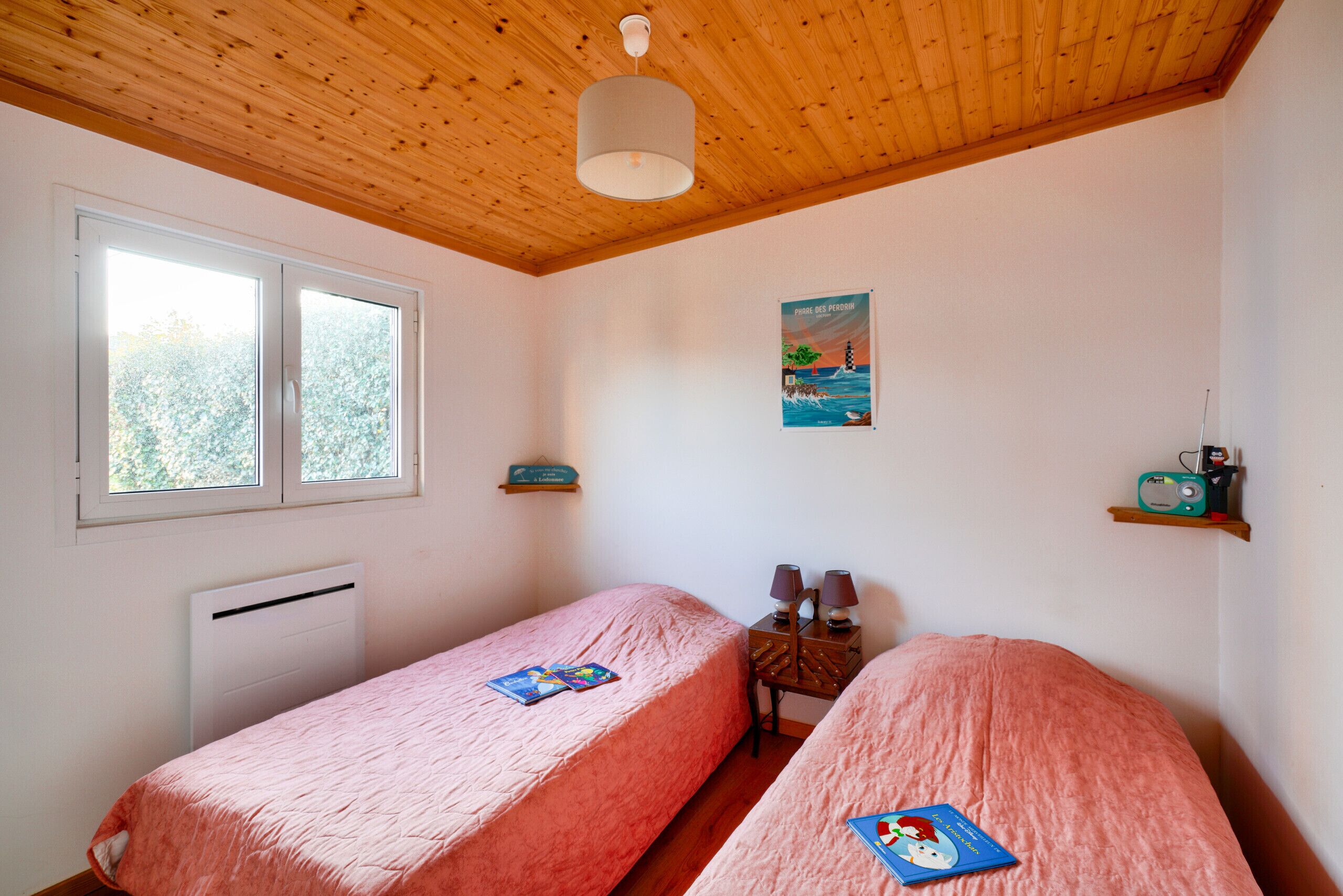 A bedroom with two beds, a radiator, a window, a painting, and a shelf with a radio.