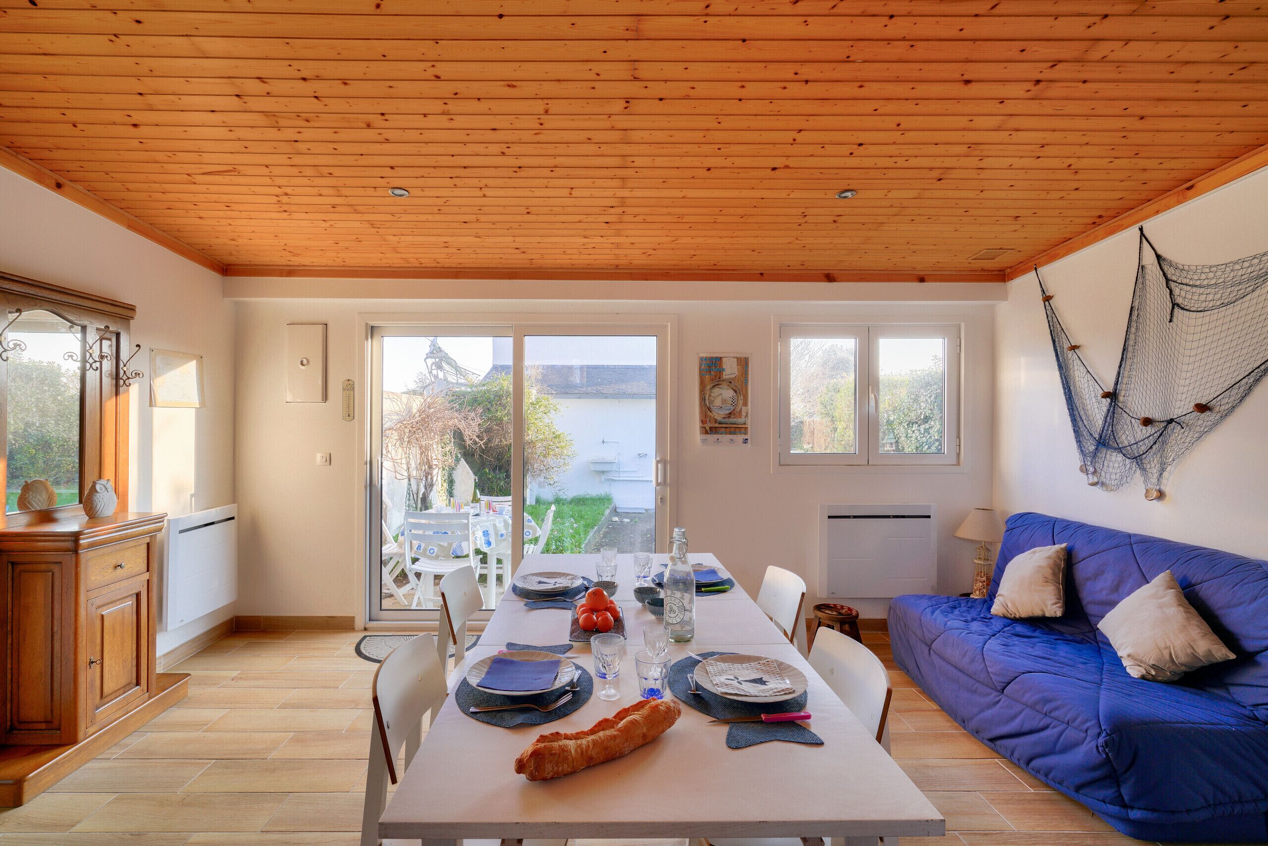 A dining area with a wooden table set for a meal, a blue sofa, and a view of the outdoors.