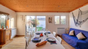 A dining area with a wooden table set for a meal, a blue sofa, and a view of the outdoors. - Chalet for 4 in Loctudy 500m from the beach (Loctudy)
