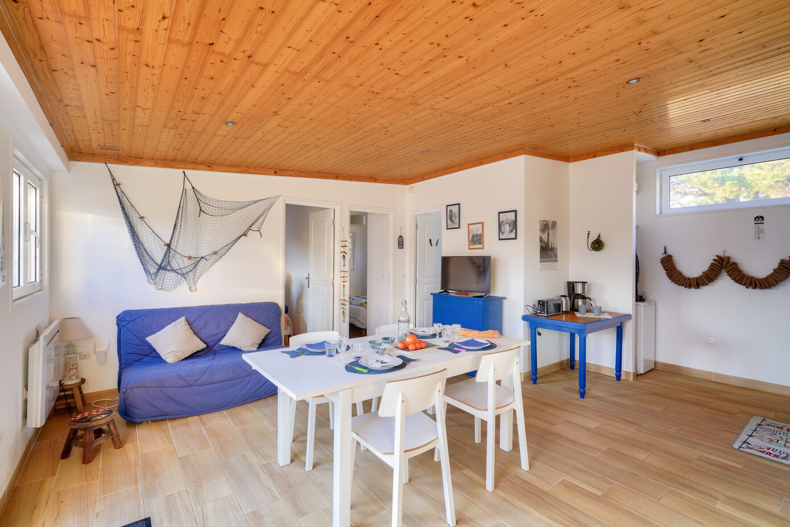 Une pièce chaleureuse avec un plafond en bois, un canapé bleu, une table à manger avec des chaises et un petit coin cuisine.