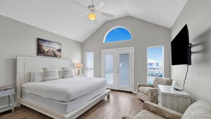 A bedroom with a bed, a ceiling fan, a desk, a chair, and a TV. - Gulf Shores Duplex | Shared Pool | Pet Friendly Beach Retreat (Gulf Shores)