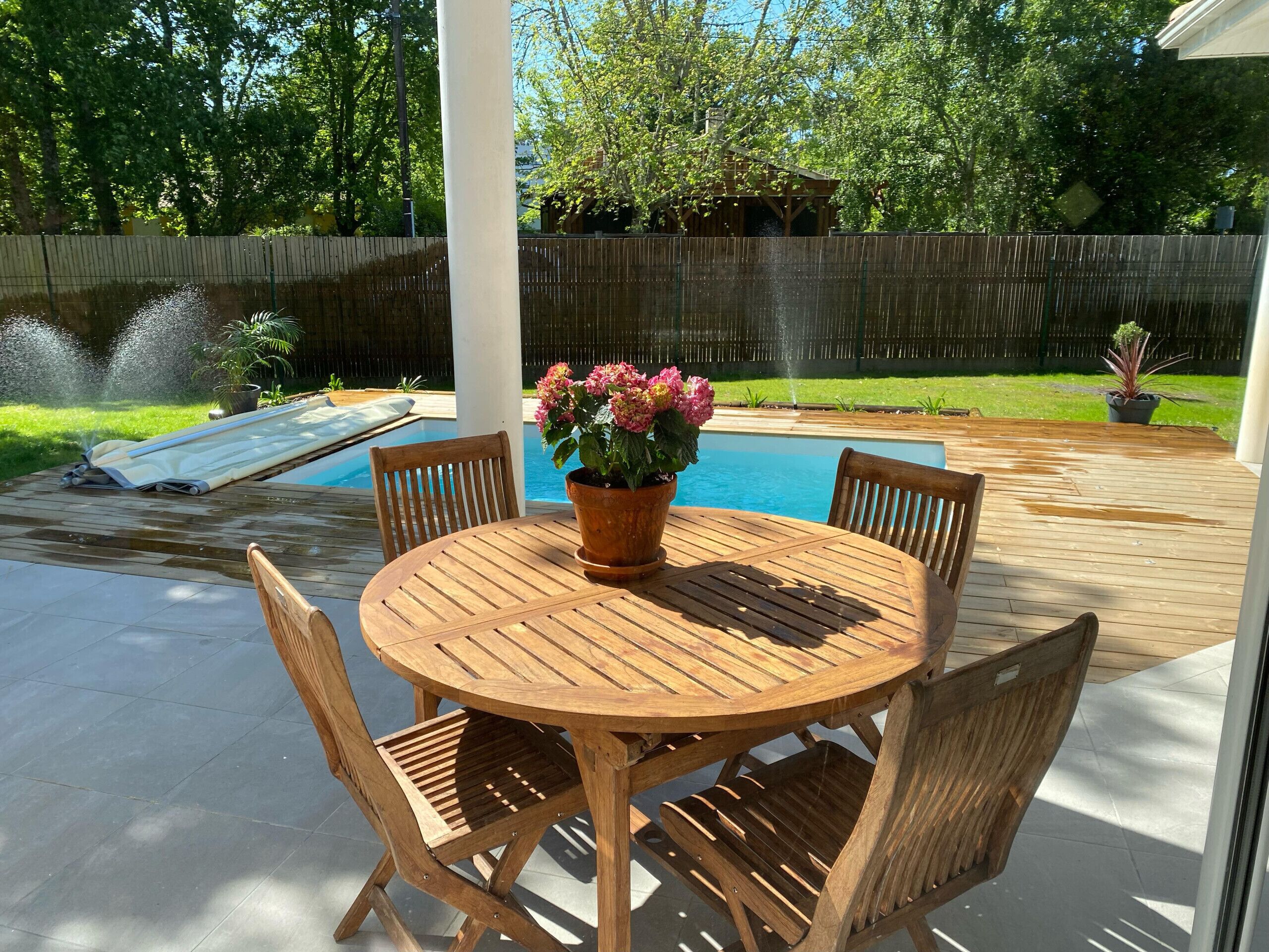 A wooden outdoor patio with a round table and chairs, a small pool, and a fountain.