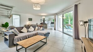 A modern living room with a sofa, coffee table, and a view of the kitchen and outdoor area. - House for 6 -Pool - 150m from the beach in Arès (Arès)