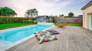 A swimming pool with a wooden deck, two colorful cushions, and a small outdoor seating area. - House with pool for 8 - 500m from the beach (Plobannalec-Lesconil)
