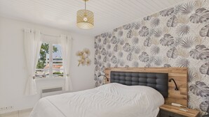Ein Schlafzimmer mit Bett, Nachttisch, Wandlampe und einem Fenster mit Vorhängen.