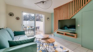 Ein modernes Wohnzimmer mit einer Couch, zwei kleinen Tischen, einem an einer Holzplatte montierten Fernseher und einer Treppe.