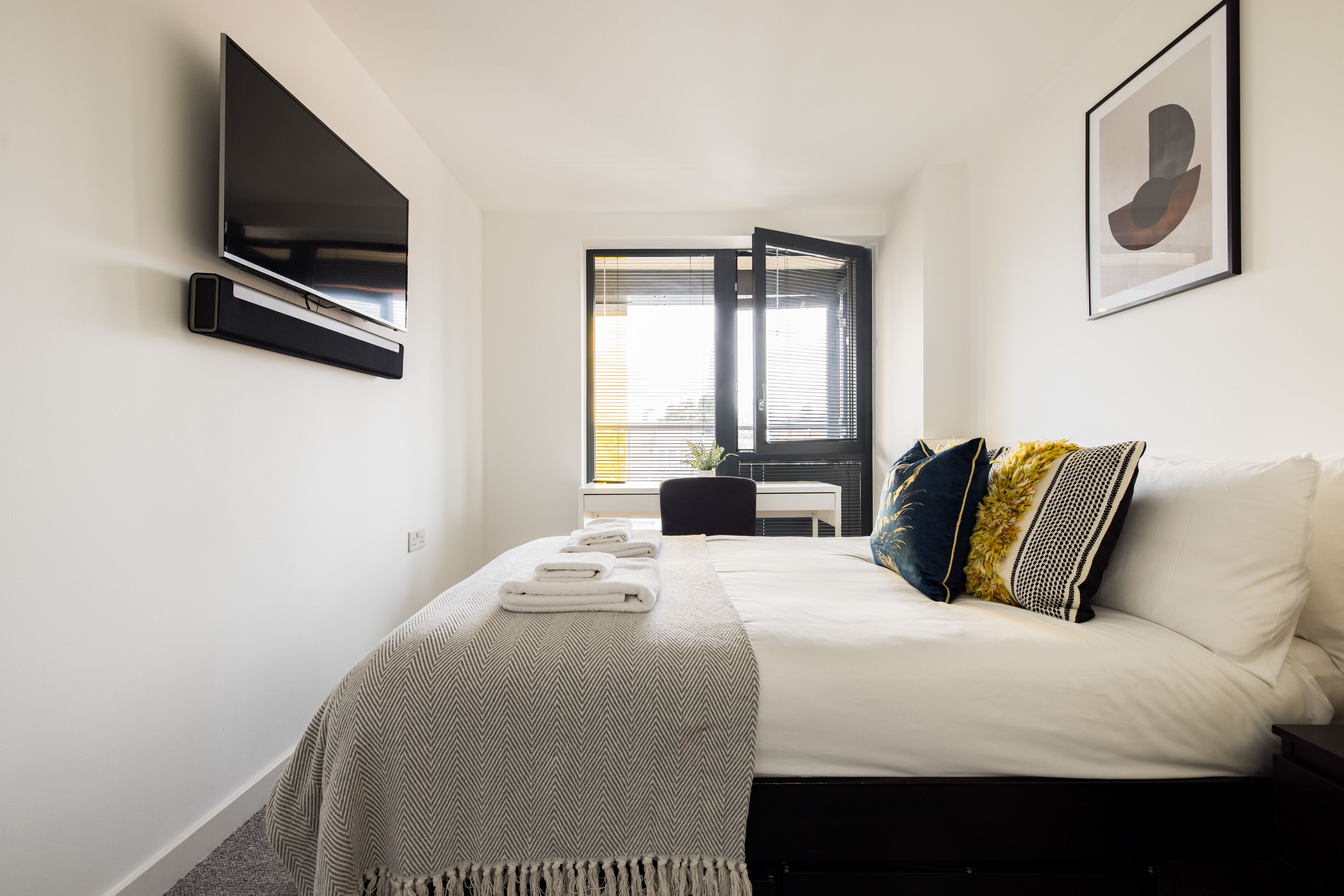 Une chambre d’hôtel moderne équipée d’un lit, d’un téléviseur fixé au mur, d’un bureau et d’une fenêtre avec des stores.