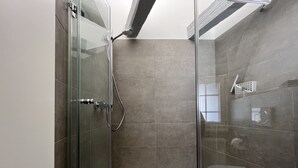 Eine moderne Dusche mit Glastür, Handbrause und integriertem Wasserhahn.