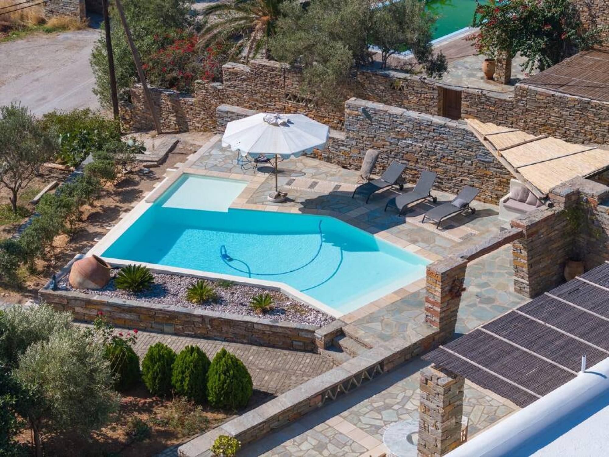A swimming pool with lounge chairs and an umbrella, surrounded by stone walls and greenery.