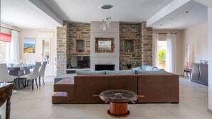 A modern living room with a stone fireplace, a large L-shaped sofa, and a dining area with a table and chairs.