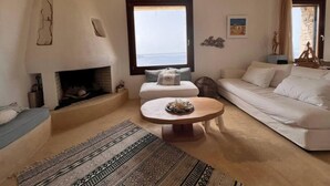 A cozy living room with a fireplace, a large window with a view, a white sofa, and a round coffee table. - Holiday House - Koundouros Panoramic Sea View (Kea)