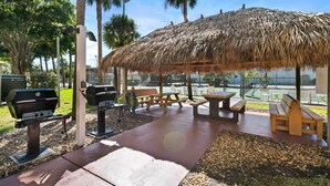 Un patio al aire libre con techo de paja, mesas de picnic y parrillas.