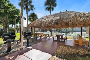 Un patio al aire libre con techo de paja, mesas de picnic y parrillas.