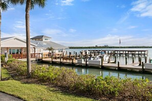 A marina with docked boats, a grassy area with palm trees, and a building with a sloped roof.