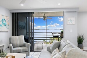 A modern living room with a view of the sea, a ceiling fan, and a dining area with a table and chairs.