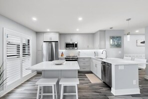 Een moderne keuken met witte kasten, roestvrijstalen apparatuur en een centraal eiland met barkrukken.