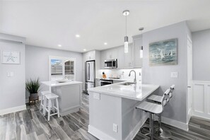 A modern kitchen with white cabinetry, a central island, stainless steel appliances, and a pendant light.