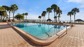 Una piscina con un borde de baldosas, rodeada de palmeras y sillones de descanso.