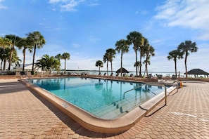 Una piscina con un borde de baldosas, rodeada de palmeras y sillones de descanso.
