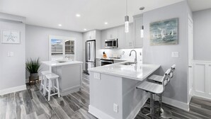 Une cuisine moderne avec des meubles blancs, un îlot central et un coin repas équipé d’une banquette.