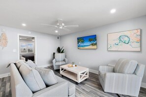 A modern living room with a sofa, armchairs, a coffee table, and a ceiling fan.