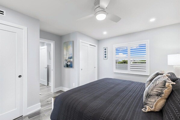 A bedroom with a bed, a ceiling fan, a window with blinds, and a door.