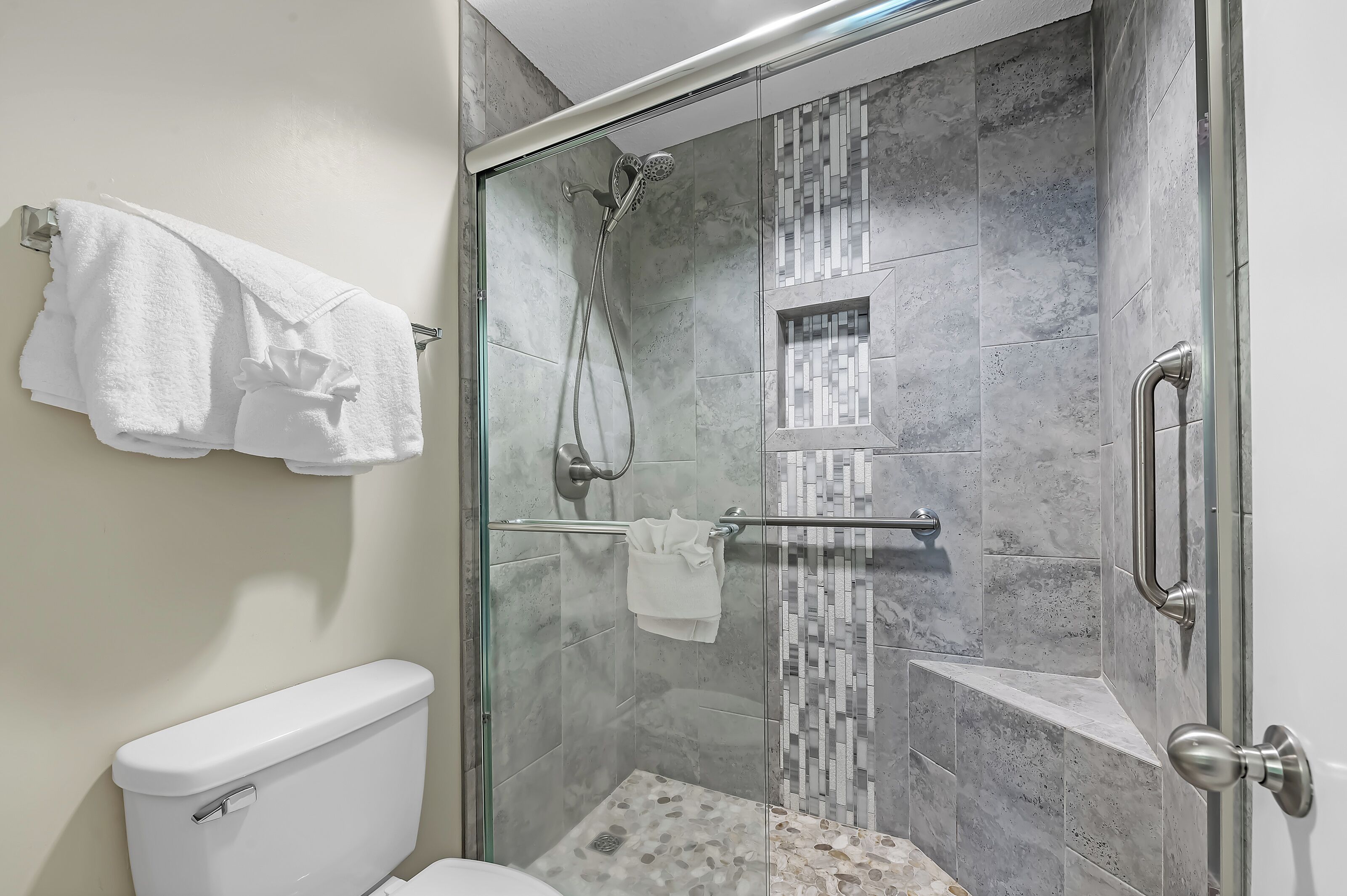 A modern bathroom with a glass-enclosed shower, a toilet, and a towel rack with towels.