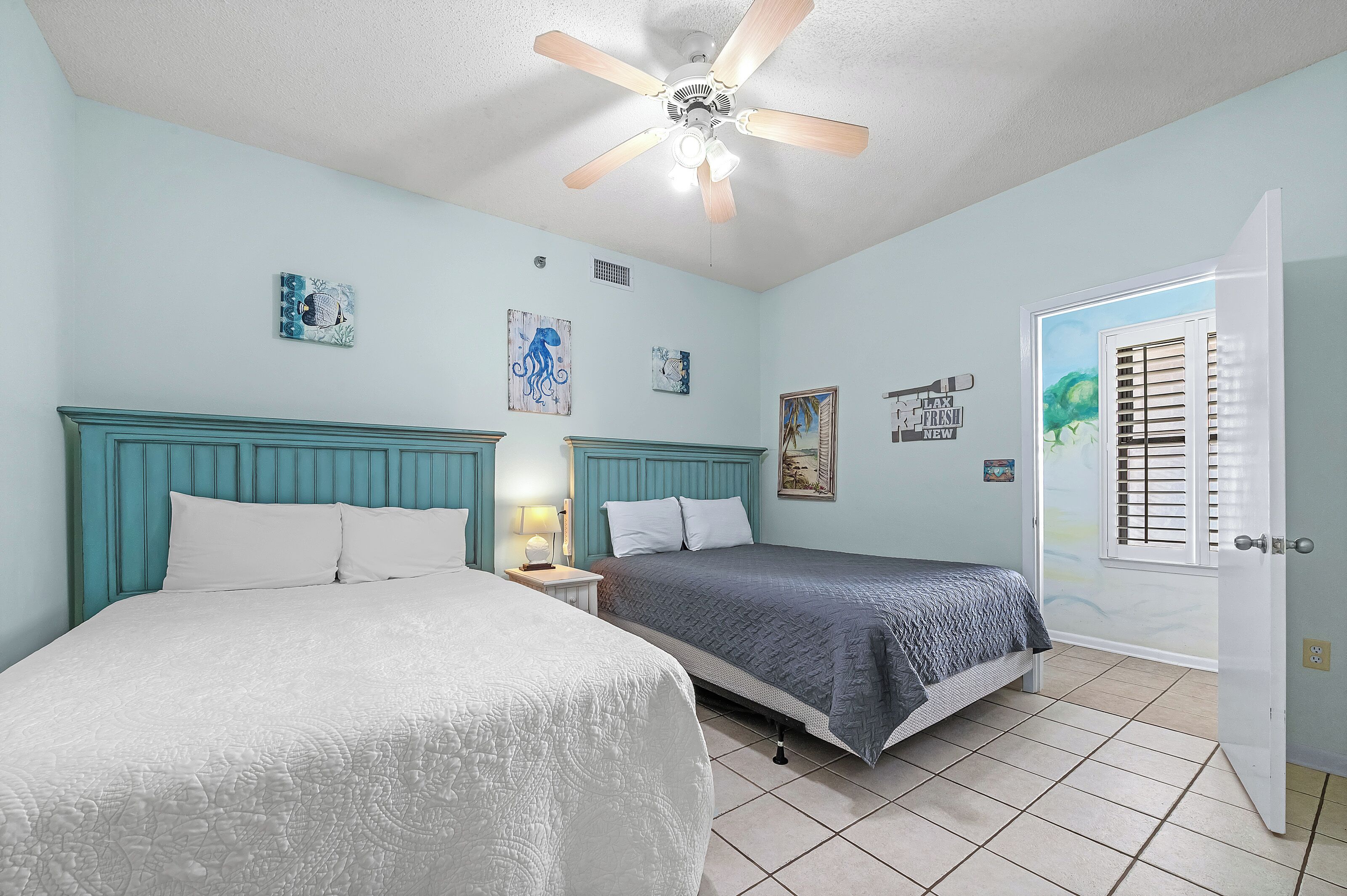 A bedroom with two beds, a ceiling fan, and artwork on the walls.