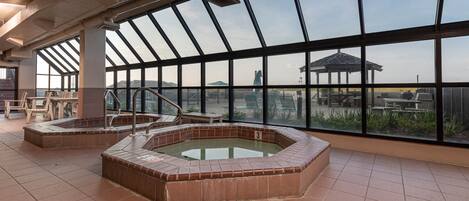 A large indoor pool area with clear views of the surrounding landscape, including a gazebo and distant hills.