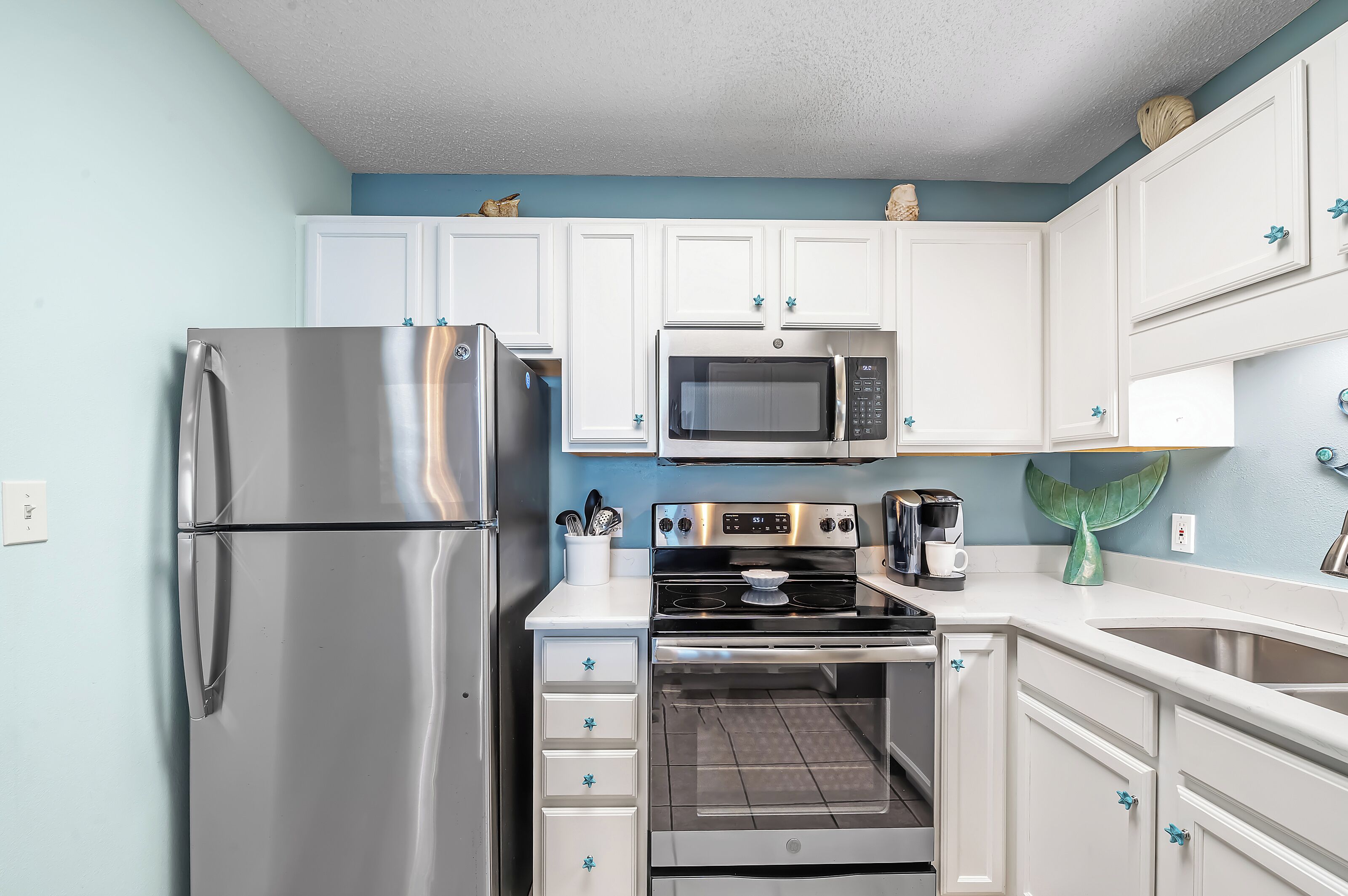 A kitchen with white cabinets, stainless steel appliances, and a teal accent wall.
