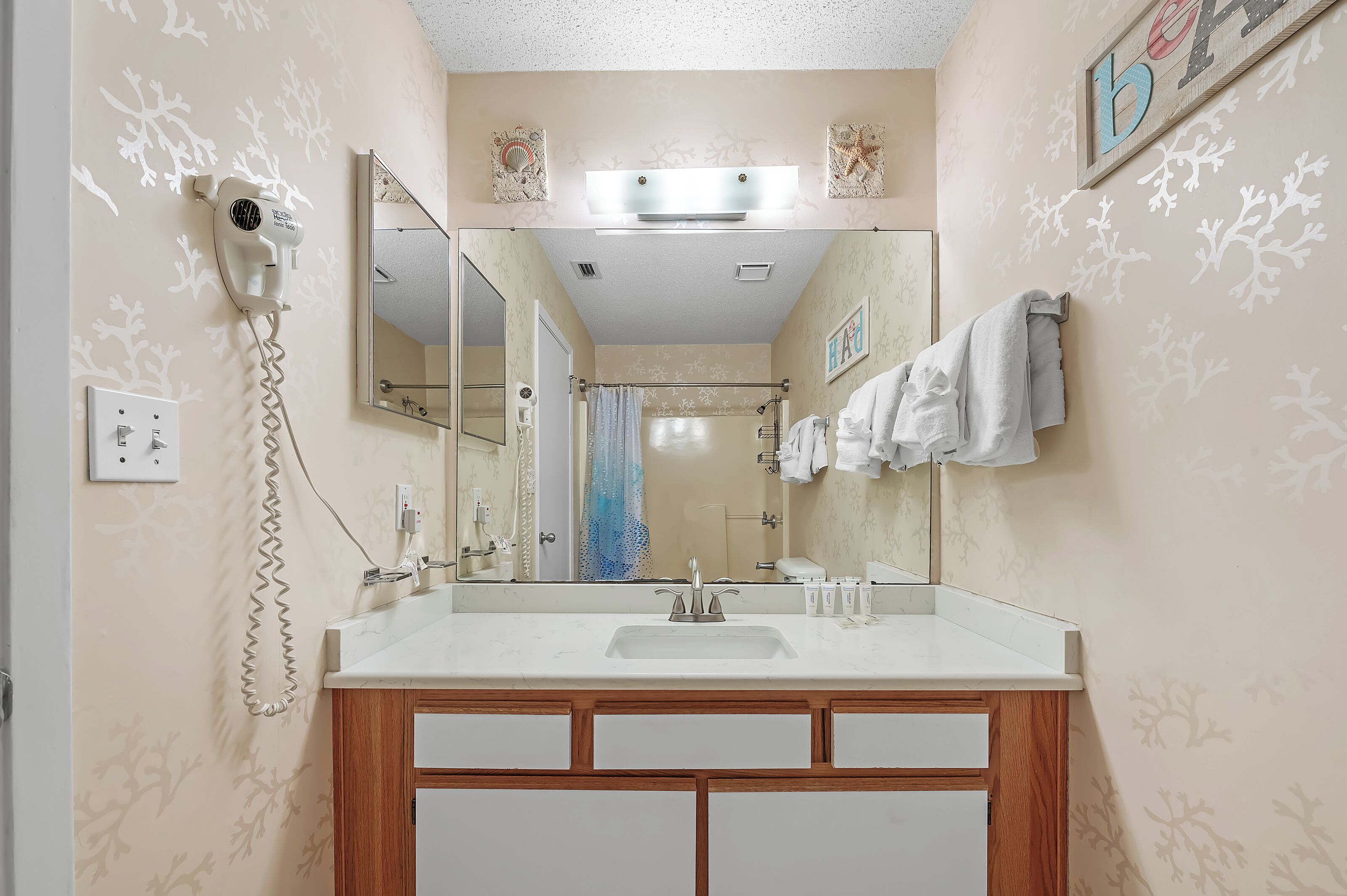 A bathroom with a large mirror, a hairdryer, a towel rack, and a shower curtain.