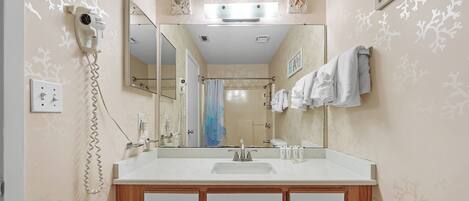 A bathroom with a large mirror, a hairdryer, a towel rack, and a shower curtain.