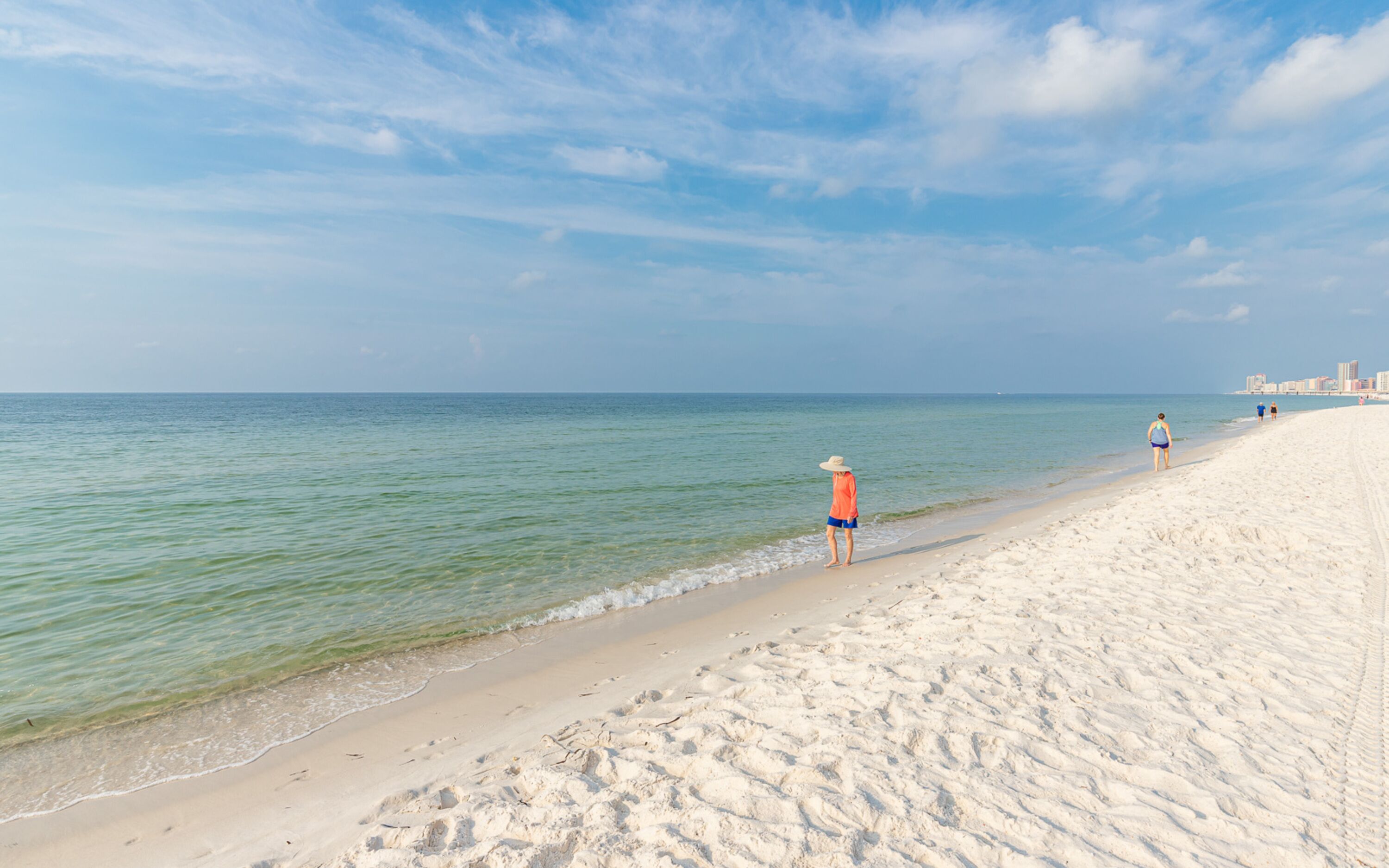 A sandy beach with clear water and a distant city skyline.