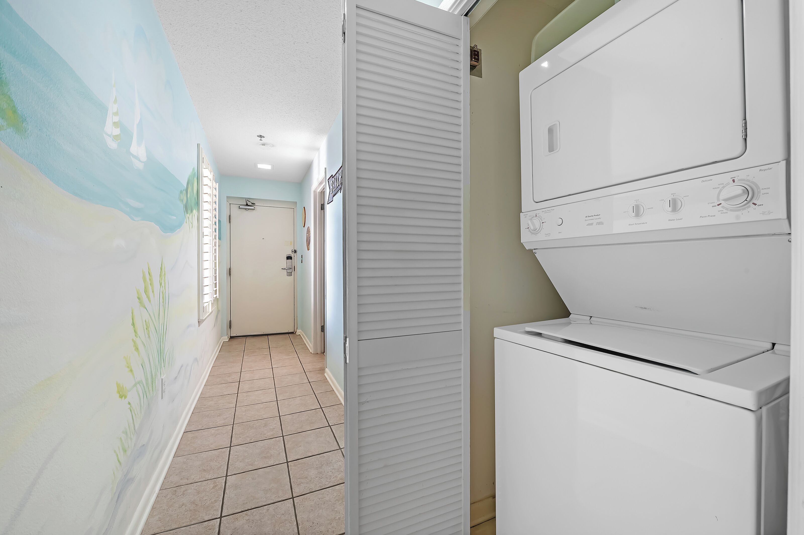 A laundry room with a white washer and dryer, a tiled floor, and a mural on the wall.